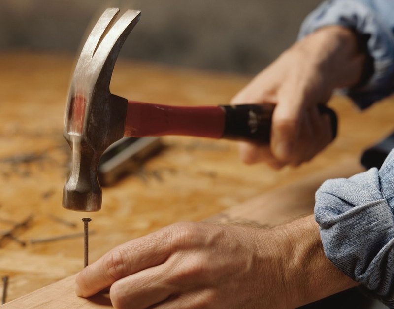Hand mit Hammer schlägt einen Nagel in Holz